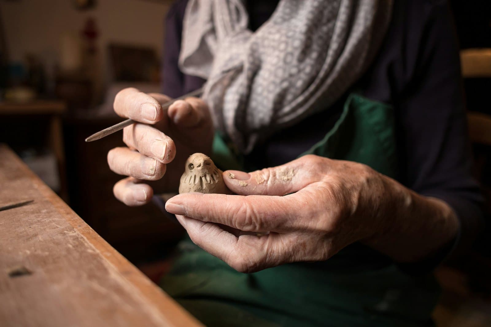 Hands carefully shaping a small wooden object in soft natural light.